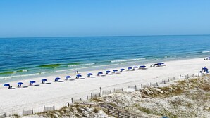 A beach with white sand, a clear blue sea, and a row of blue umbrellas along the shore. - IP 616-Completely Renovated, Luxury Ocean Front 3bdrm/3bath (Fort Walton Beach)