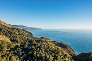 A coastal landscape with a view of the sea, a forested hillside, and a small settlement with buildings.