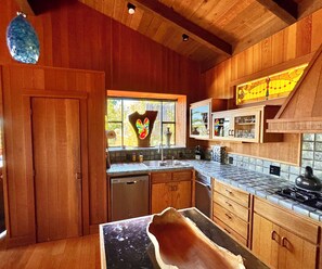 A wooden kitchen with a dishwasher, a stove, and a window with a butterfly decoration. - Central Big Sur Retreat - Pool, Spa, Guest House + 5 Acres (Big Sur)