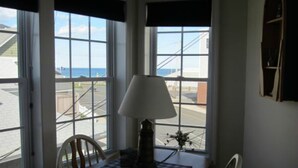 Une pièce avec vue sur la mer, grâce à de grandes fenêtres, comprenant un fauteuil, une lampe et une petite table.