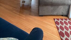 Un salon avec un canapé gris, une table à manger avec des chaises, un ventilateur de plafond et une fenêtre avec des stores.