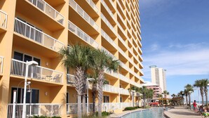 Une piscine entourée d’un immeuble de grande hauteur doté de balcons, de palmiers et surplombant un ciel dégagé.