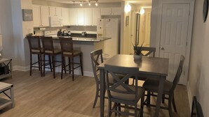 Une cuisine compacte avec des meubles blancs, un îlot central et des tabourets de bar.