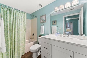 Un baño con cortina de ducha, bañera, inodoro, lavabo y tocador con cajones.