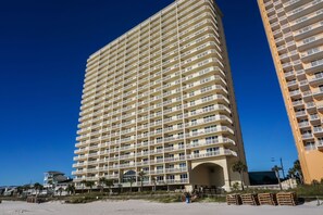 Un hotel moderno de gran altura con varios balcones, vista a la playa y una entrada destacada.