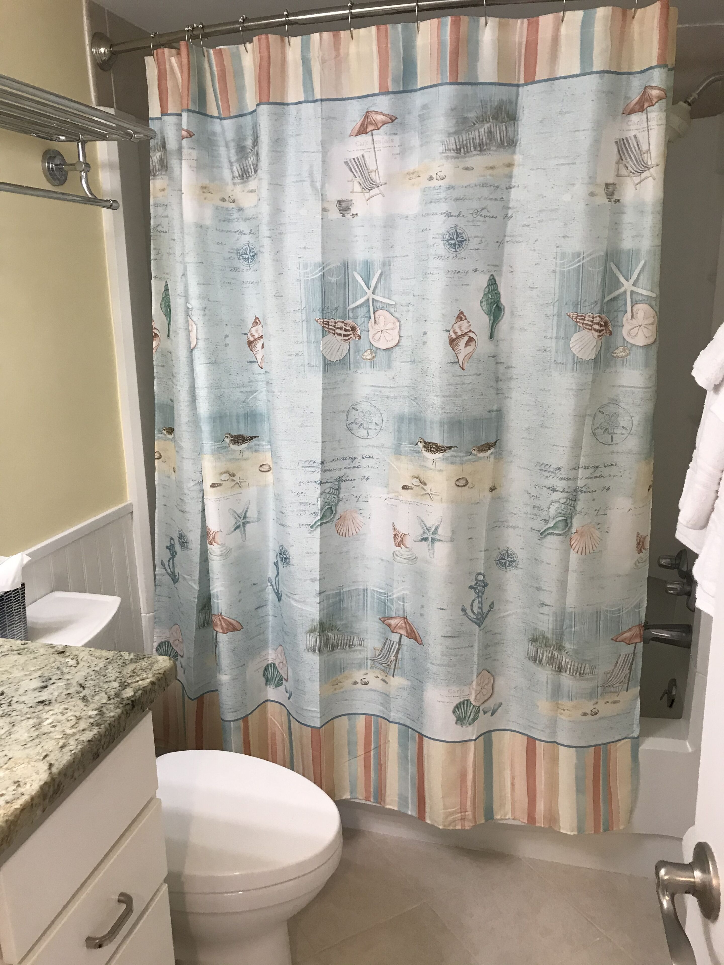 A bathroom with a striped shower curtain, a white toilet, a granite countertop, and a towel rack.