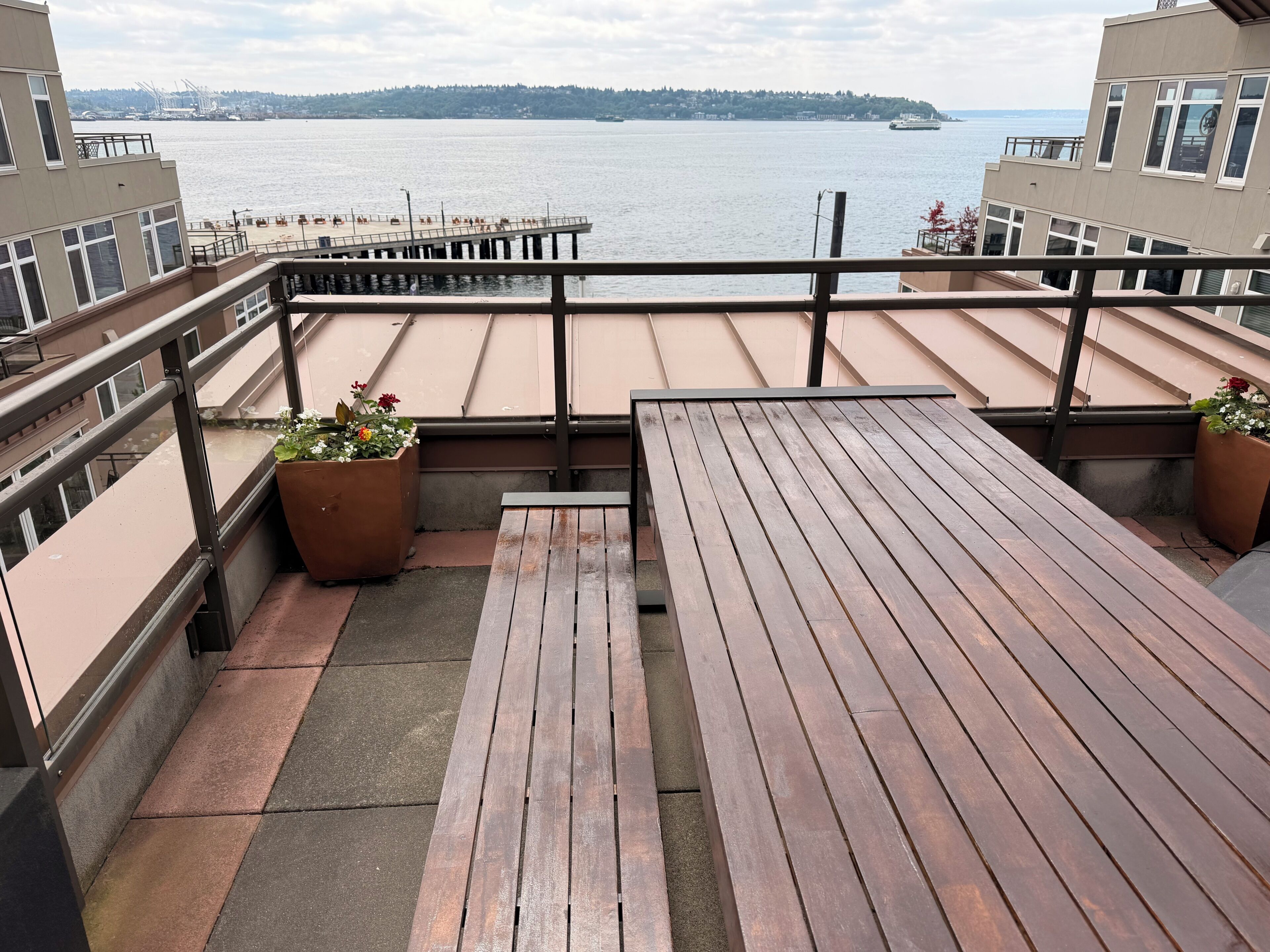 A balcony with a view of the water, wooden benches, and potted plants.