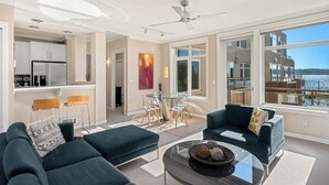 Una sala de estar moderna con un sofá verde oscuro, una mesa de centro de cristal y vistas a un paisaje urbano a través de amplias ventanas.