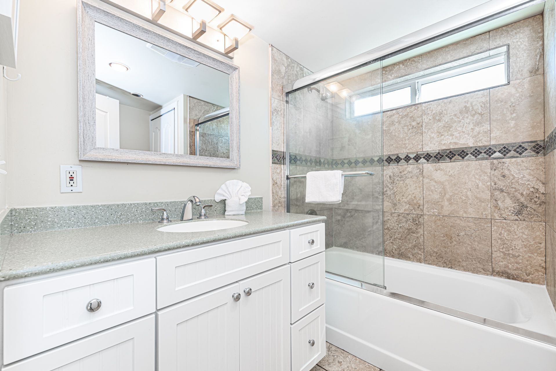 A modern bathroom with a glass-enclosed shower, a large mirror, and a granite countertop.