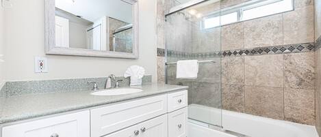 A modern bathroom with a glass-enclosed shower, a large mirror, and a granite countertop.