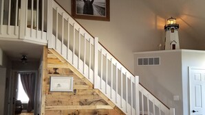 A staircase with wooden steps and white railings, leading to a second floor. A framed picture hangs on the wall above the staircase. - Ocean Retreat -  Rustic style house  w/pool, Pet Friendly.  (Rehoboth Beach)