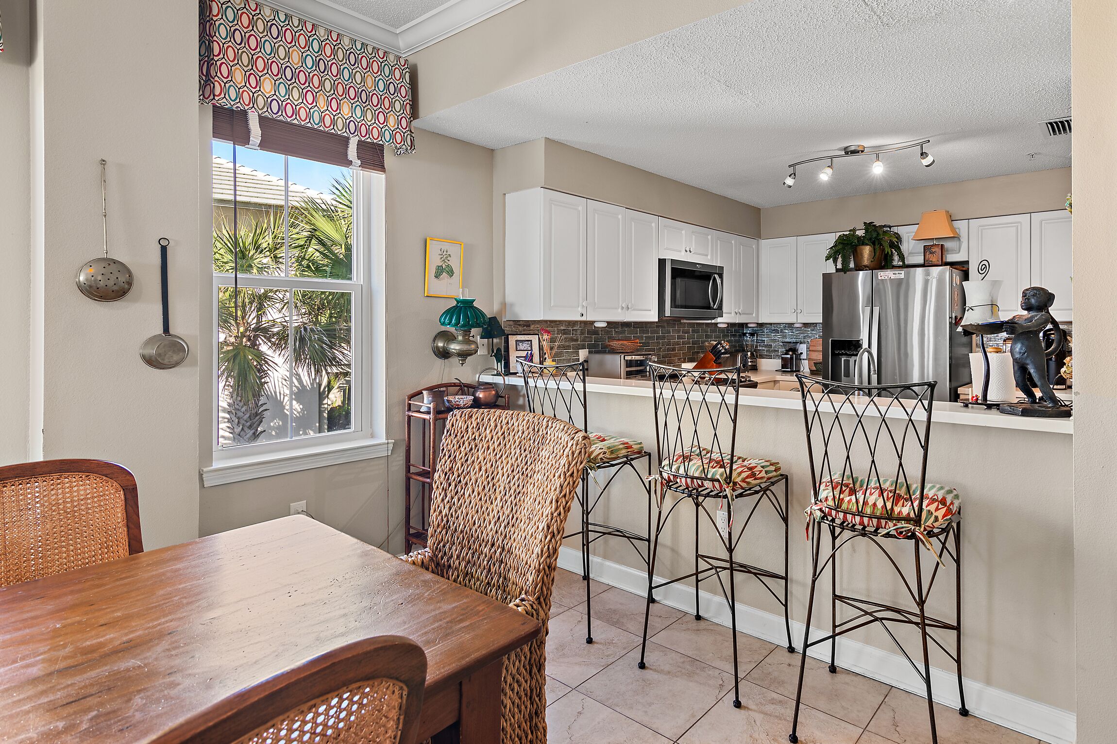 A kitchen with white cabinets, a stainless steel refrigerator, and a dining area with wicker chairs and a wooden table.