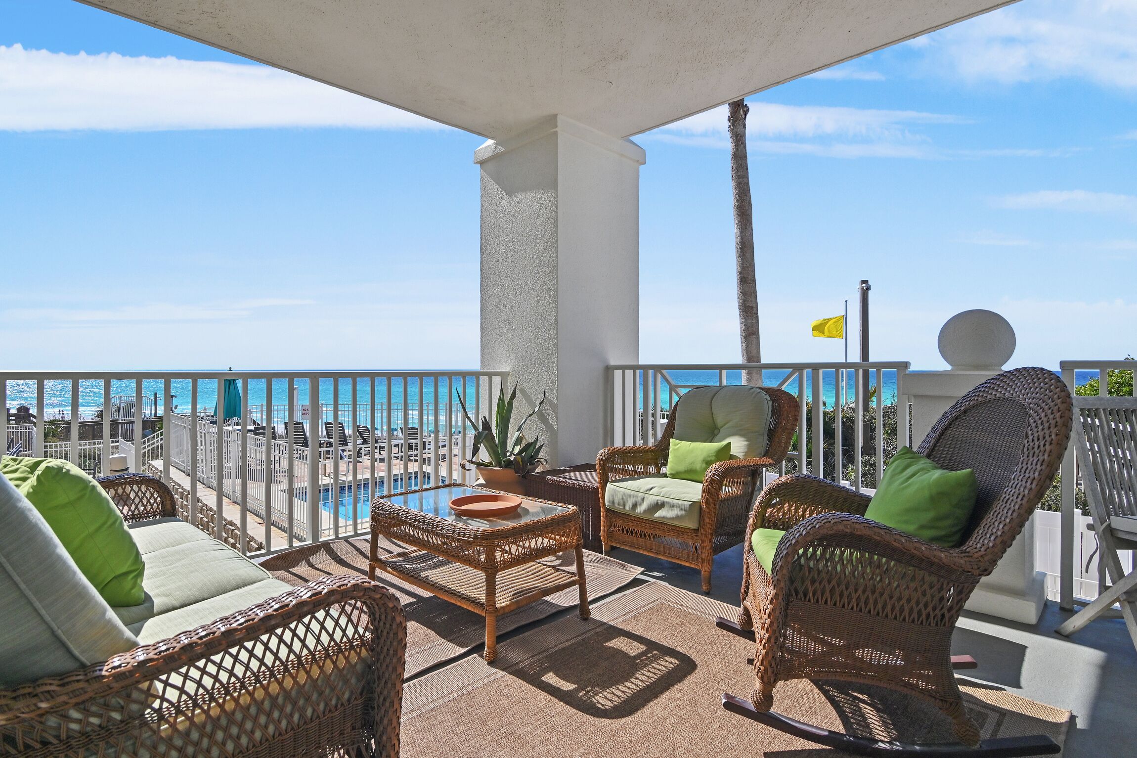 A balcony with wicker furniture, a view of the sea, and a flag.