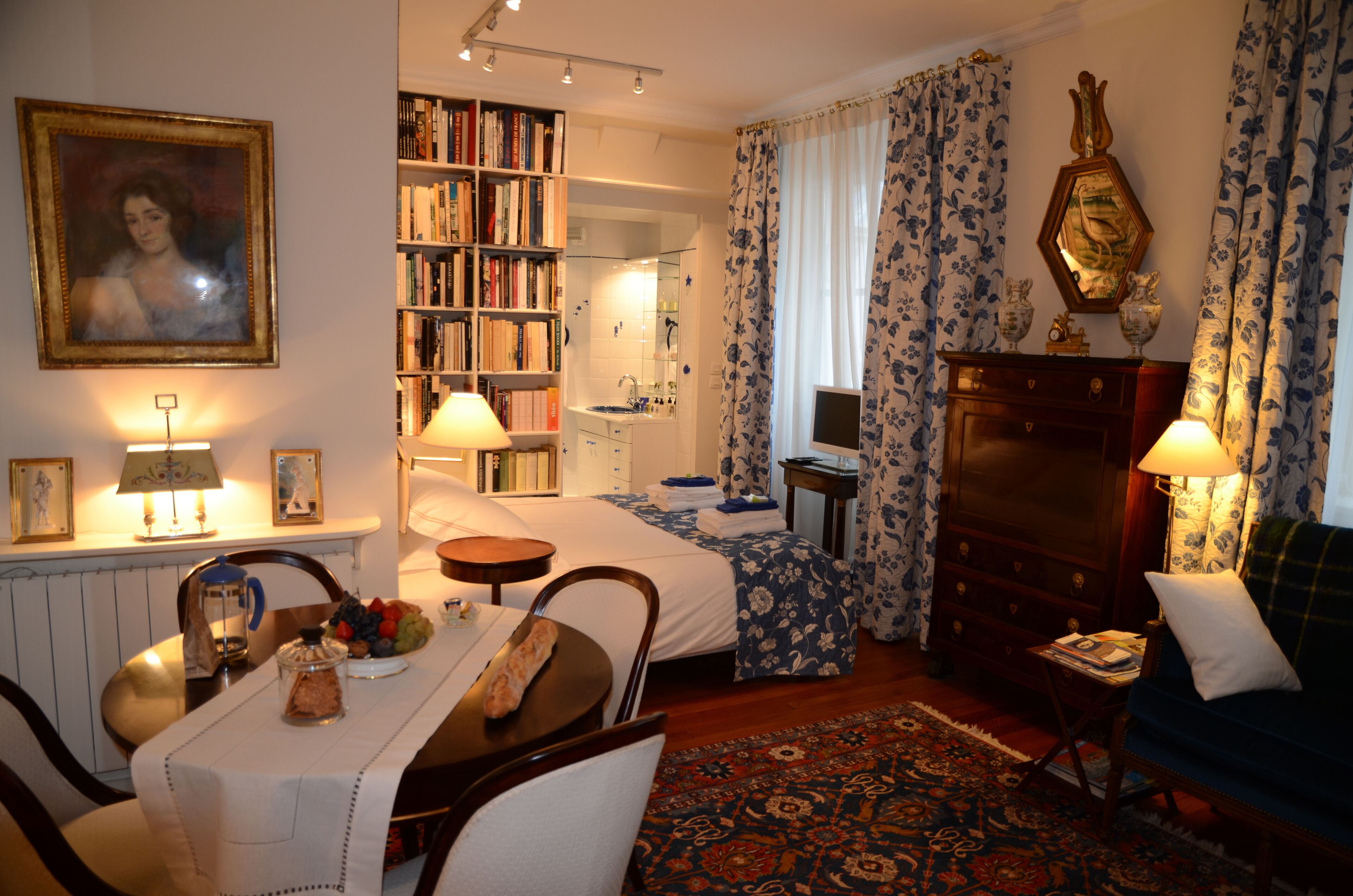 Une chambre d’hôtel bien éclairée, avec un lit, un bureau doté d’une lampe, une bibliothèque, une commode et un canapé.