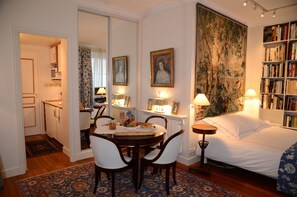 A bedroom with a bed, bedside table, lamp, and a bookshelf. - Elegant studio in Palais- Royal Monument, next to Le Louvre (Paris)