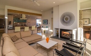 A modern living room with a sectional sofa, a coffee table, and a fireplace. There is a dining area with a table and chairs in the background.