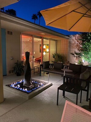 An outdoor patio with a fire feature, seating, and a large umbrella. - Luxury Midcentury Modern   (Palm Desert)