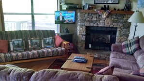 Ett vardagsrum med en stenbeklädd öppen spis, en tv som är monterad på väggen och en soffa med mönstrade kuddar.