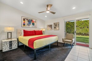 A bedroom with a bed, two bedside tables, a ceiling fan, and a view of a garden through a sliding door.