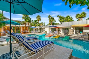 A pool area with lounge chairs and umbrellas, surrounded by palm trees and a clear sky.