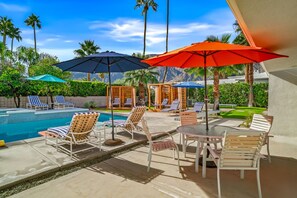 A poolside area with lounge chairs, umbrellas, and a table.
