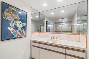 A bathroom with a large mirror, a sink, and a framed artwork on the wall.