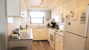 A compact kitchen with white cabinets, a stainless steel sink, and a refrigerator with magnets.