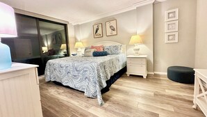 A bedroom with a bed, bedside tables, a nightstand, a mirror, and framed pictures on the wall.