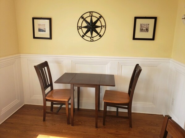 Un coin repas avec une table en bois et deux chaises, des tableaux encadrés au mur et une décoration en forme de boussole.
