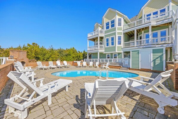 A pool area with lounge chairs and a two-story building with balconies. - Premier Semi-Oceanfront Home w/ Pool, Elevator, Hot Tub, Game Room, and Theater (Salvo)