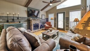 A cozy living room with a stone fireplace, leather sofa, and a ceiling fan. - Family Getaway Close to Parkway-w/ Theater and Game Room (Pigeon Forge)