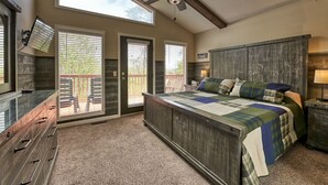 A bedroom with a large bed, a ceiling fan, a TV mounted on the wall, and a view of the outside through the windows. - Family Getaway Close to Parkway-w/ Theater and Game Room (Pigeon Forge)