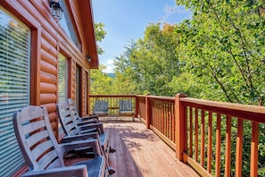 A wooden deck with chairs and a railing, overlooking a forested area. - Family Getaway Close to Parkway-w/ Theater and Game Room (Pigeon Forge)