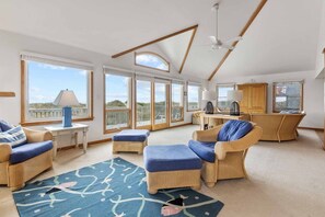 A spacious living area with wicker furniture, large windows, a ceiling fan, and a view of the outdoors. - Oceanfront Home in Waves with Hot Tub, Grill, and Screened Porch (Waves)