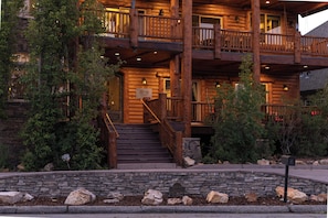 A log cabin-style hotel with a stone foundation, wooden balconies, and a stone staircase leading to the entrance.