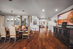 A spacious dining area with a wooden floor, a chandelier, and a large painting on the wall. - 🐻🏰 The Big Bear Castle | Luxury 6,000 Sq Ft • 6BR/7BA • Hot Tub • Lakeview! (Big Bear)