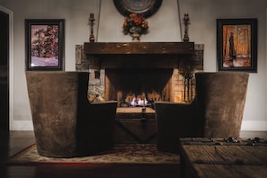 A fireplace with a stone mantle, two upholstered chairs, and framed artwork on the walls.