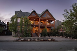 A large log cabin with a prominent front porch, multiple levels, and a stone foundation.