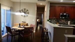 Una cocina moderna con un microondas de acero inoxidable, un lavamanos y una encimera. Hay una zona de comedor con una mesa y sillas de madera.