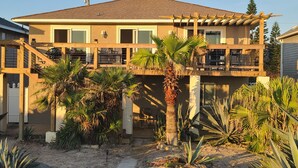 A two-story house with a balcony, surrounded by palm trees and other vegetation.