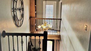 A staircase with a black railing, a decorative wall clock, and a hanging light fixture.