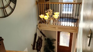 A wooden staircase with a black railing, a chandelier, and a ship's wheel decoration.