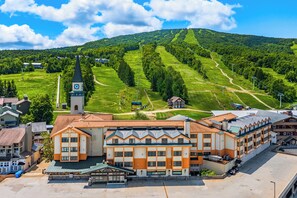 A hotel with a prominent clock tower, surrounded by lush green hills and a clear sky.