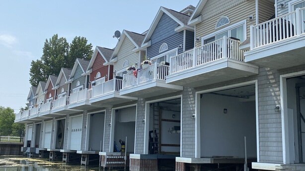 Une rangée de chalets situés au bord de l’eau, dotés de balcons, dont certains sont pourvus de garages attenants, et un plan d’eau paisible en premier plan.