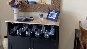 Une pièce avec un miroir, un décor représentant un gouvernail de navire, un meuble à bouteilles et une petite table sur laquelle se trouvent un cadre photo et une lampe.