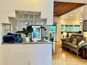 A modern living room with a wooden ceiling, a built-in shelving unit, a sofa, and a dining area visible through an open door.