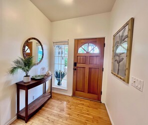 A hallway with a wooden door, a console table with a potted plant, a mirror, and a framed picture on the wall.