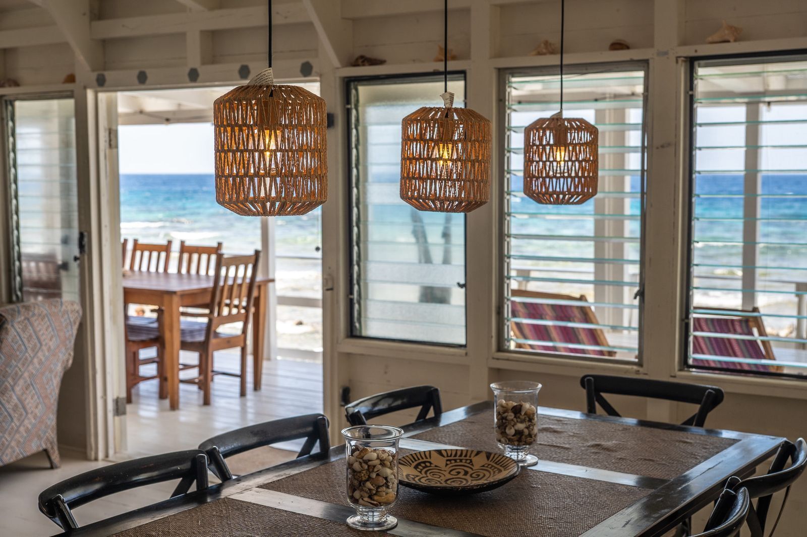 A dining area with wicker pendant lights, a table set with a plate, a glass of nuts, and a pitcher.