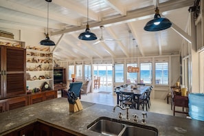 A spacious kitchen with a large island, multiple hanging lights, and a view of the ocean through large windows. - Ocean Breeze Villa: Oceanfront, Private Dock & Pool, Sleeps 16, Pet Friendly (Roatan)