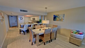 A modern kitchen with white cabinets, a central island, and a dining area with wicker chairs and a white table.